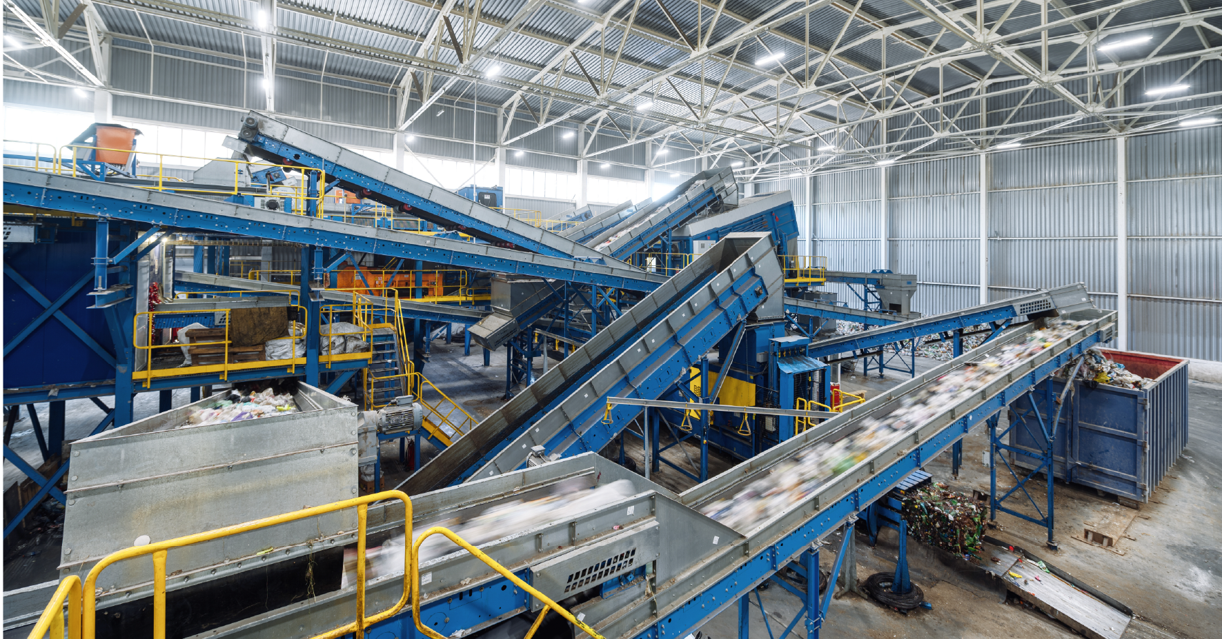 Industrial recycling facility with blue conveyor belts sorting materials under metal warehouse ceiling structure.