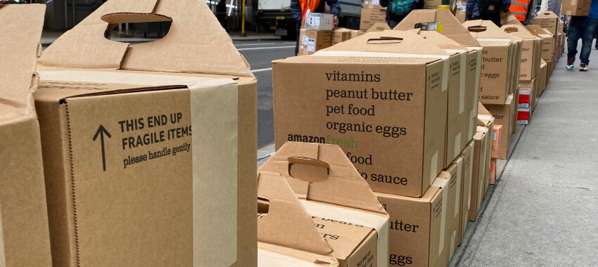 Rows of cardboard boxes labeled with food items like vitamins, peanut butter, and organic eggs are lined up outside for delivery or pickup.