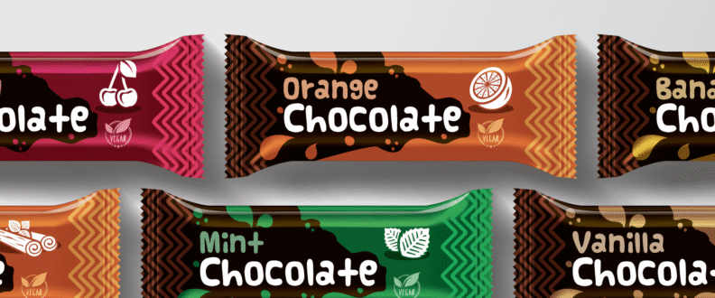 Colorful flexible candy bar wrappers in cherry, orange, mint, cinnamon, banana, and vanilla chocolate flavors arranged on gray background.