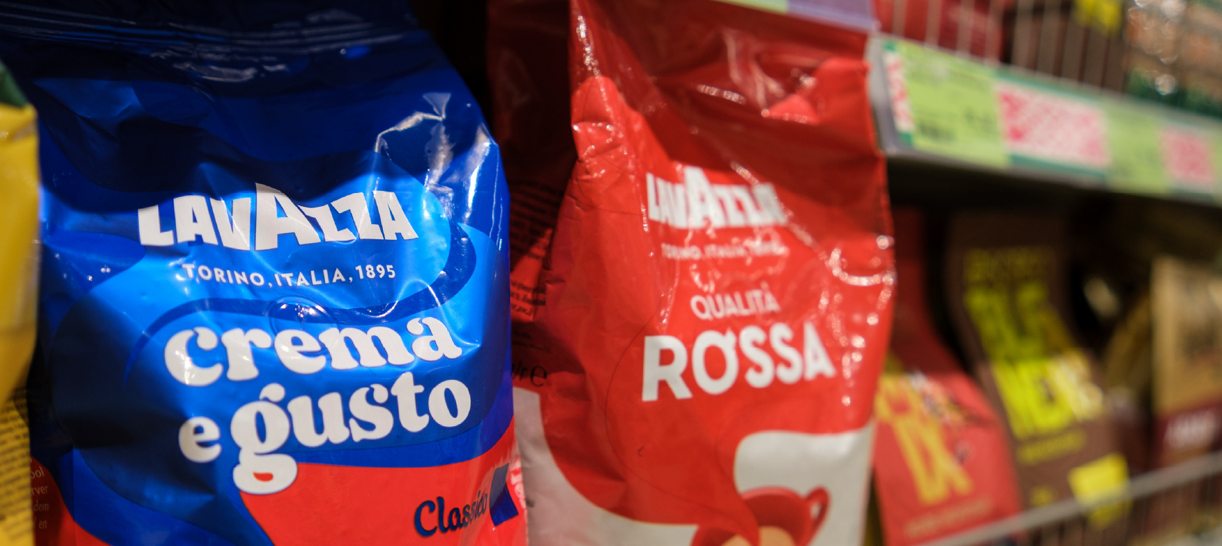 Two Lavazza coffee bags in blue and red flexible packaging displayed on a retail store shelf.