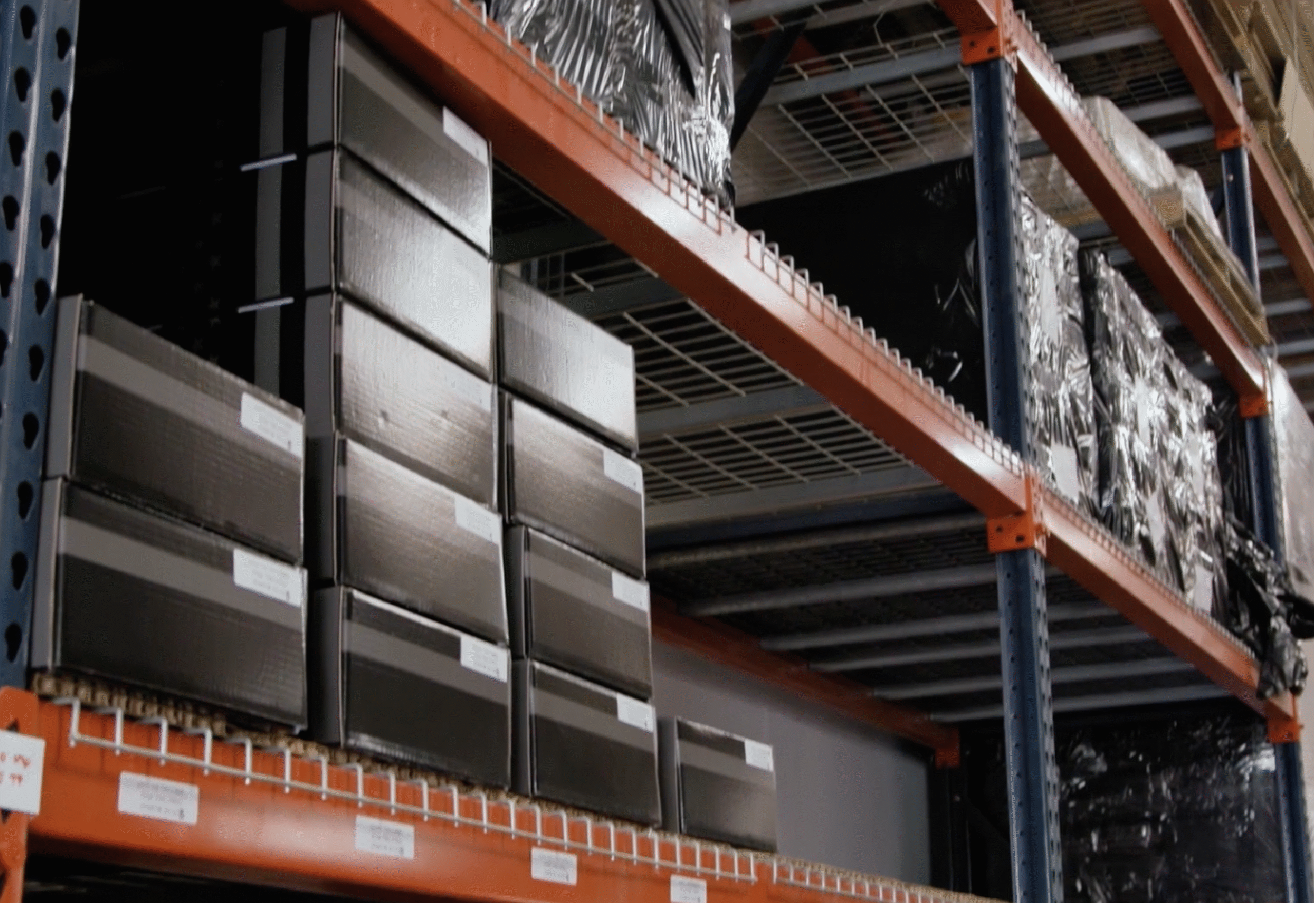 Industrial warehouse shelving system with organized metal drawer units and wrapped pallets on orange racking.