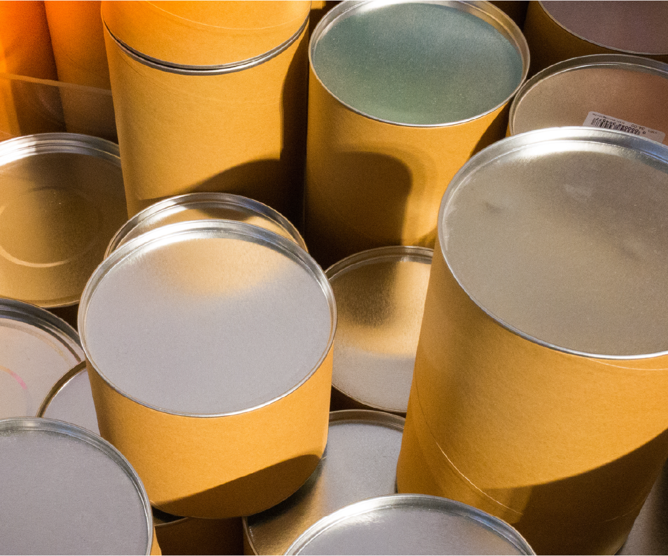 A cluster of plain kraft cardboard tubes with silver metal lids grouped together, viewed from above at an angle, bathed in warm golden light.