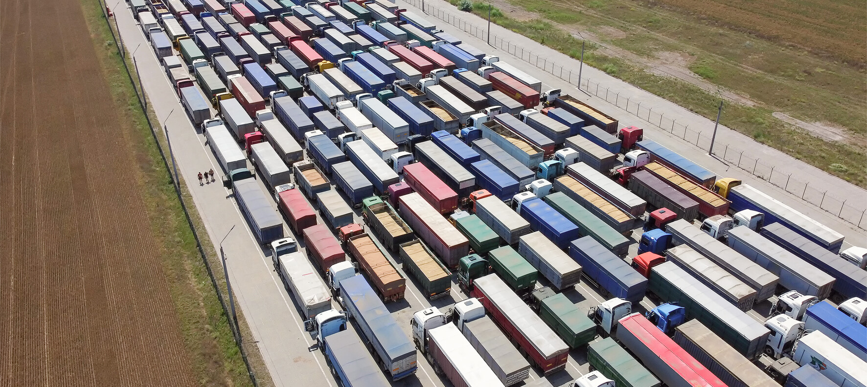 Aerial drone view of hundreds of colorful semi-trucks and trailers packed tightly in rows in a large commercial lot or border crossing.