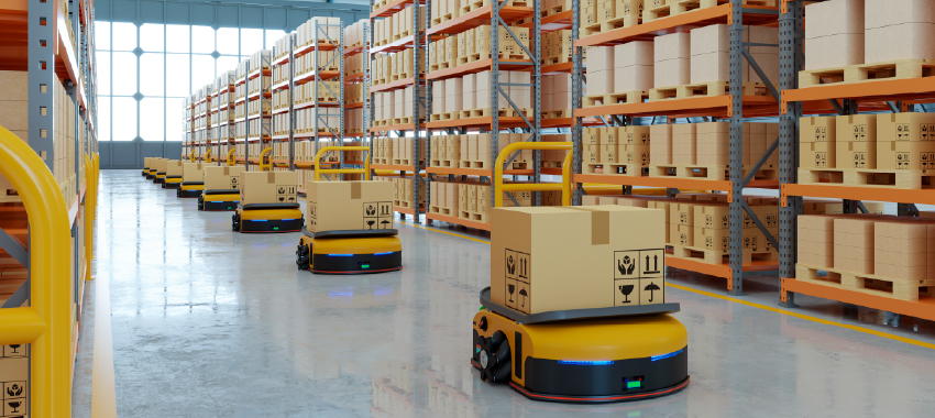 A row of yellow autonomous mobile robots transports cardboard boxes down a wide aisle lined with tall warehouse shelving racks.