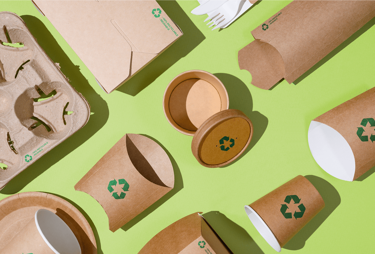 An assortment of kraft paper recyclable packaging items labeled with green recycling symbols arranged on a bright green background.