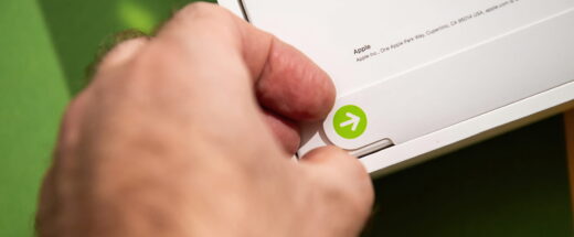 A hand opens an Apple product box, revealing a green arrow sticker on white packaging.