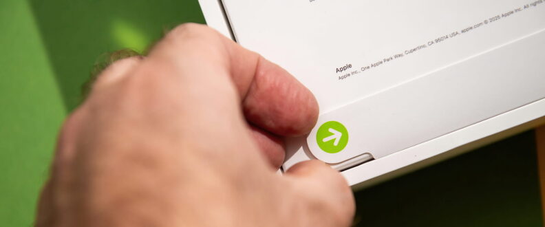 A hand opens an Apple product box, revealing a green arrow sticker on white packaging.