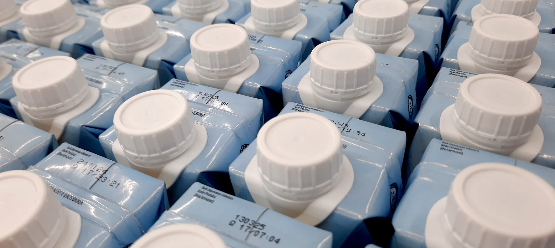 Rows of blue beverage cartons with white screw caps, stamped with production codes.
