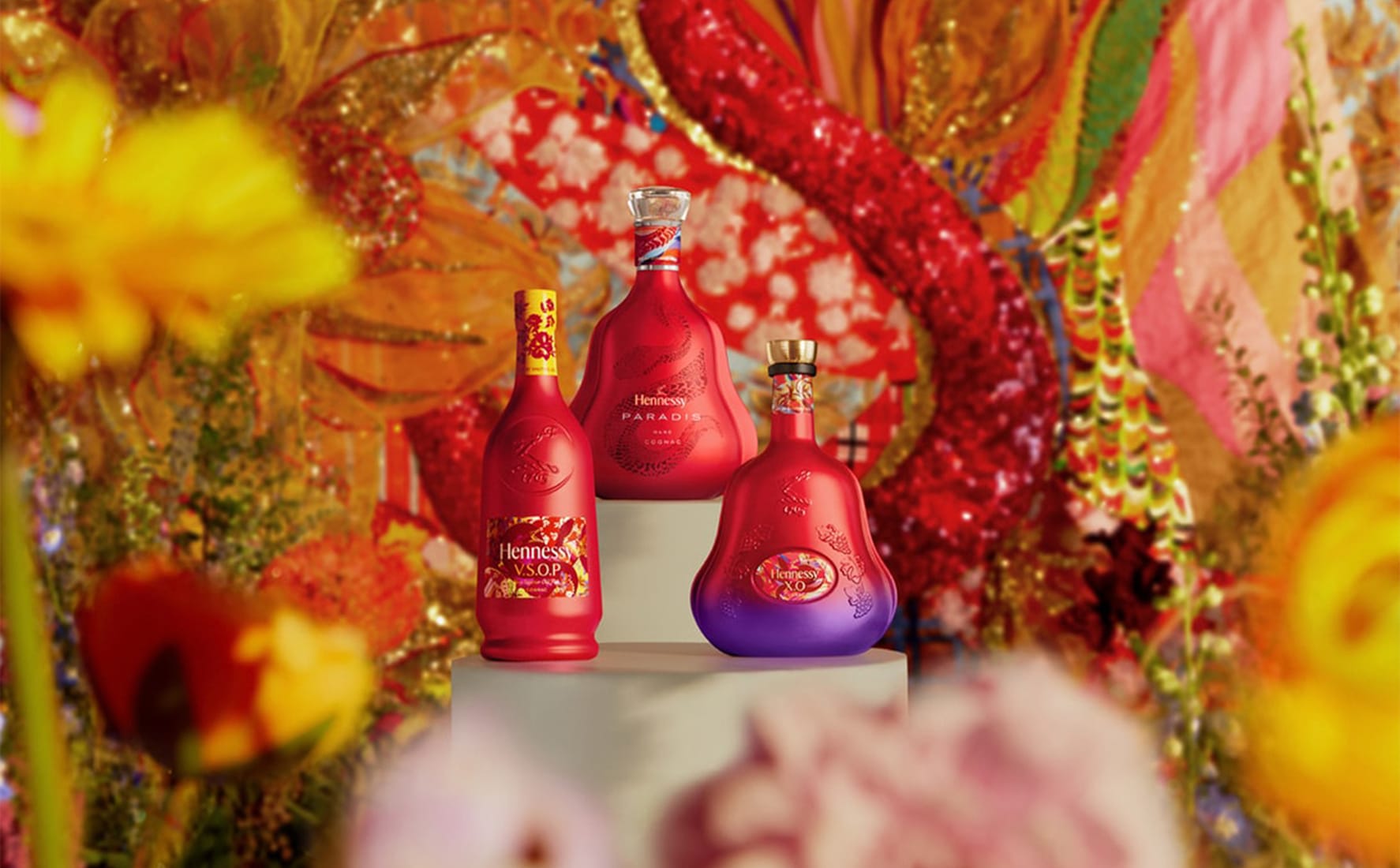 Hennessy V.S.O.P., Paradis, and X.O. cognac bottles in limited edition red and purple packaging for Lunar New Year, staged against a vibrant floral backdrop.