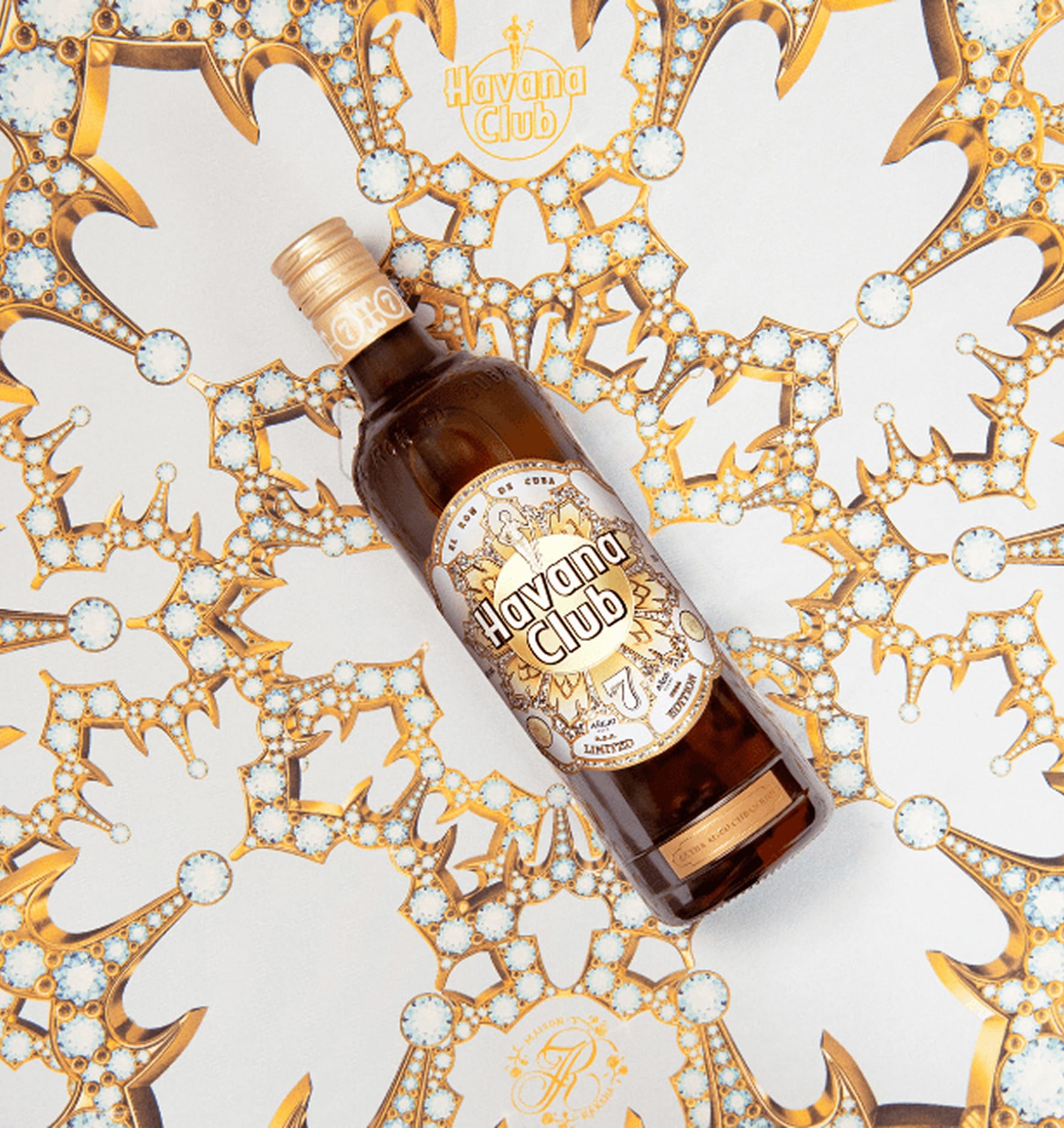 A Havana Club 7 Year limited edition rum bottle laid flat on a surface printed with an intricate gold and white geometric pattern matching the bottle's label design.