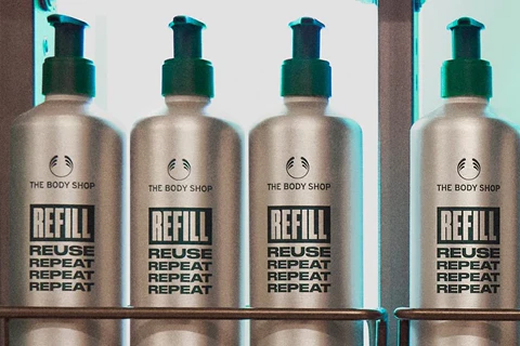Four reusable aluminum pump bottles with The Body Shop logo and the words refill, reuse, repeat, repeat, repeat