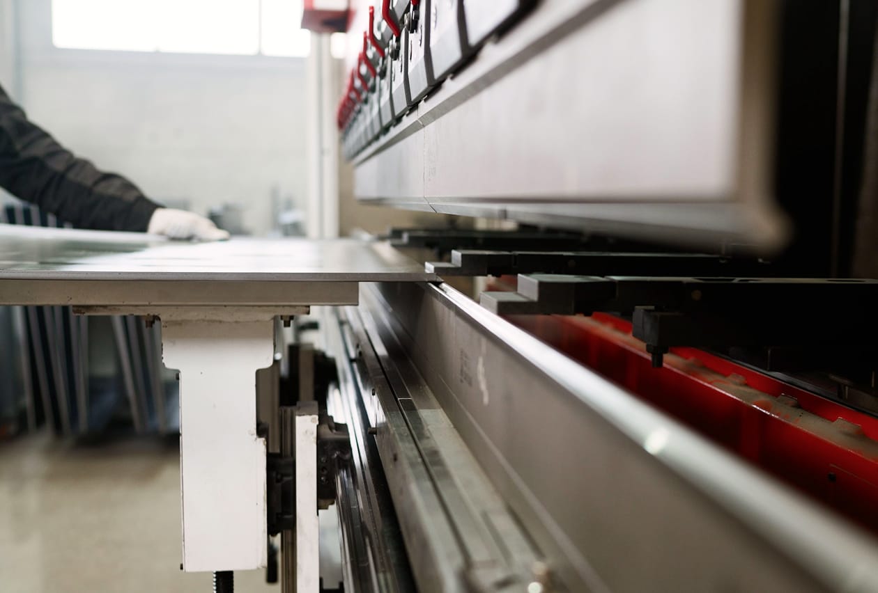 Worker operating an industrial sheet metal press brake machine on a manufacturing floor.
