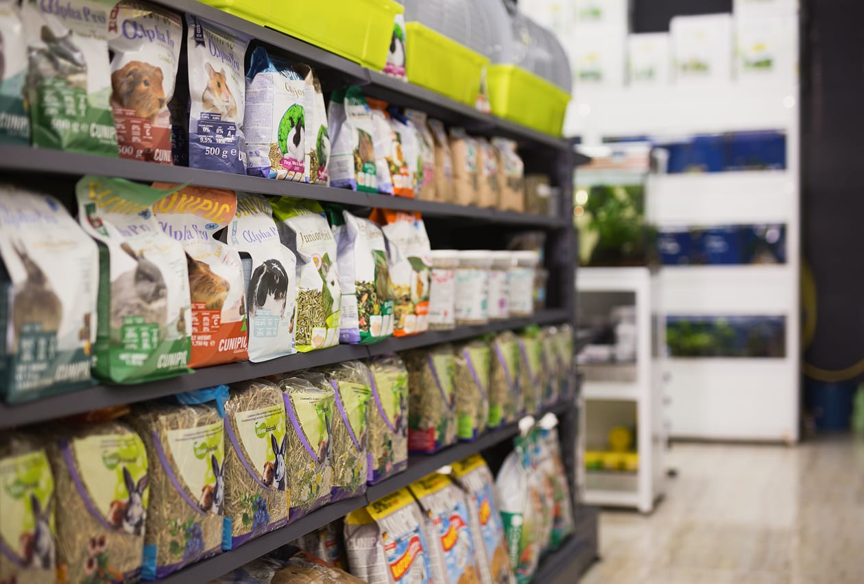 Retail pet store shelves stocked with an assortment of small animal food and hay packaging.