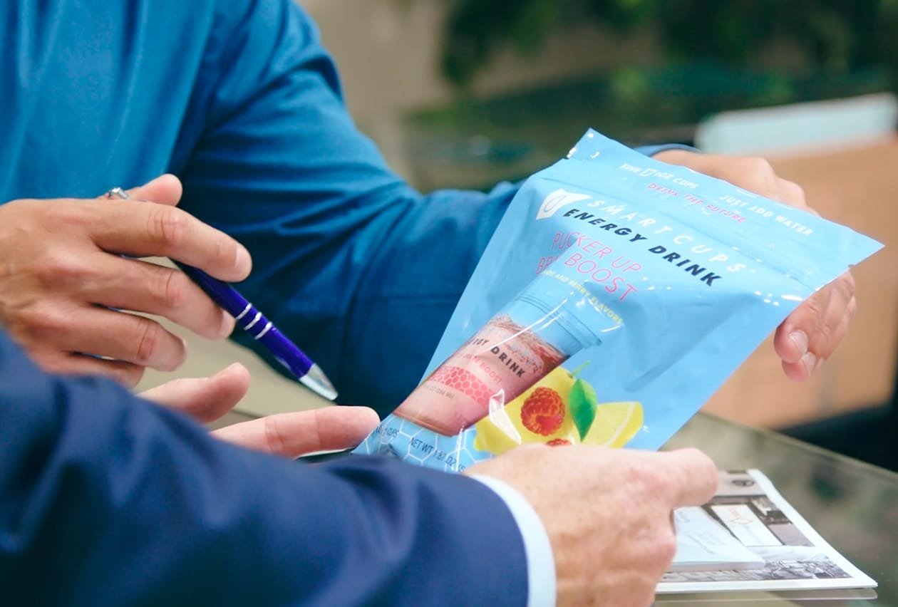 Two business professionals reviewing a SmartCups energy drink flexible packaging sample during a meeting.